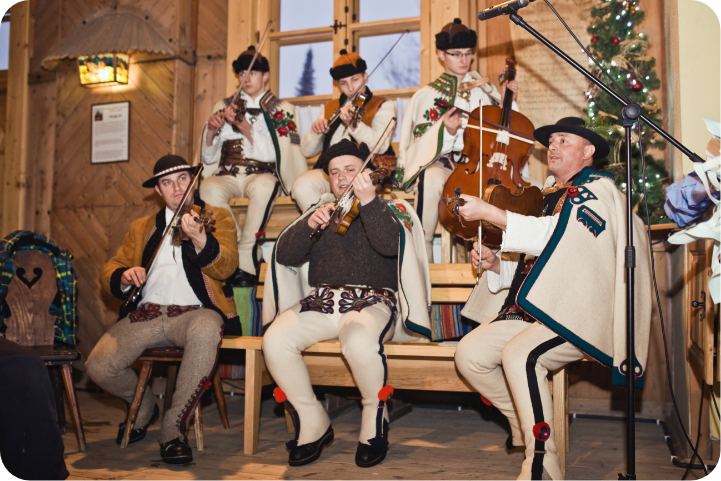Sześciu mężczyzn w strojach góralskich gra na instrumentach - pięciu na skrzypcach, jeden na basie
